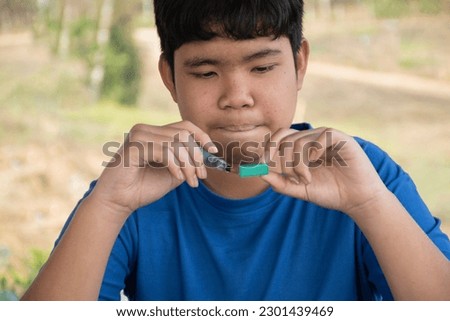 Young asian boy in blue t-shirt holding paintbrush and watercolor briquettes, sitting and drawing watercolor pictures in his freetime at home, teenager actitity and summer vacation concept.