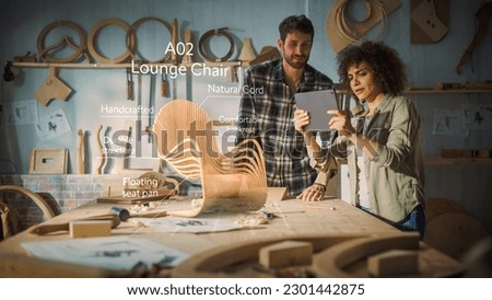 Multiethnic Female Furniture Designer Showing to Professional Male Carpenter New Chair Design On Tablet Computer. VFX 3D Hologram Edit Appears on the Work Table With Infographics, Production Info.