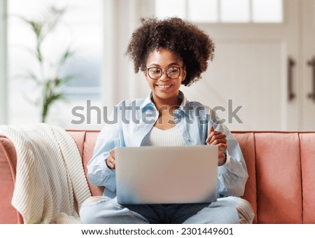 beautiful young smiling african american woman with curly hair uses laptop smiling, gesticulating and talking to online while sitting on sofa at home
 Royalty-Free Stock Photo #2301449601