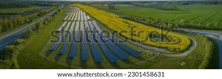 Panorama view of photovoltaics on open spaces with grazing sheeps. The solar park along highway with grazing sheeps and yellow rapeseed field. Renewable green energy. Alternative energy sources.  Royalty-Free Stock Photo #2301458631