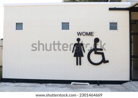 Sign of woman and wheelchair on white wall concrete of toilet building.