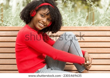 Happy Young Afro Woman Listening to Music on Park Bench and Positively Engaging with Camera