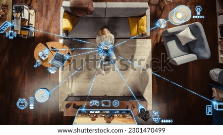 Top View Of Caucasian Woman In the Loft Apartment Sitting On Carpet Next To Couch and Connecting Smartphone to Smart Home System. VFX Edit Visualizing Connected Devices. Laptop, TV, Speaker. Royalty-Free Stock Photo #2301470499