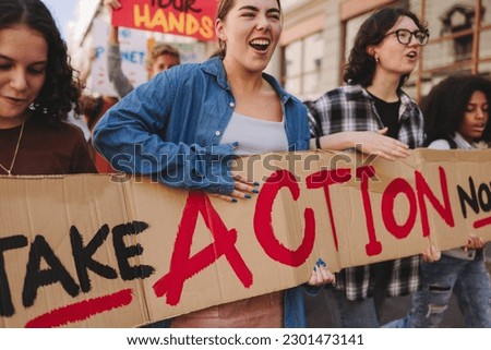 Global climate strike. Vibrant young people holding a banner while marching against climate change. Multicultural youth activists campaigning for climate justice and environmental sustainability. Royalty-Free Stock Photo #2301473141