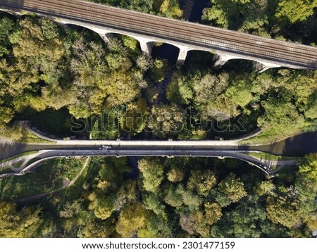 Bird's eye aerial view of Marple Viaduct and Aqueduct carrying the Hope Valley railway line and Peak Forest canal respectively, with surrounding forest and River Goyt flowing underneath Royalty-Free Stock Photo #2301477159