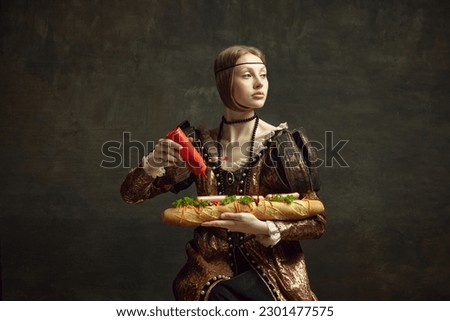 Portrait of young girl, queen, princess in vintage costume putting ketchup on giant sandwich baguette on dark green background. Concept of history, renaissance art, comparison of eras, health and food Royalty-Free Stock Photo #2301477575