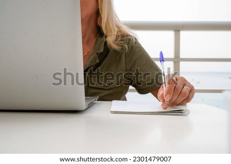 an unrecognizable left-handed woman writes in a notebook with a laptop outside. international left handers day Royalty-Free Stock Photo #2301479007