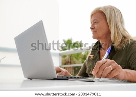 a left-handed woman writes in a notebook and working with a computer outside. international left handers day Royalty-Free Stock Photo #2301479011