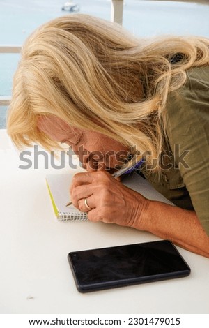 a left-handed woman with vision problems writes concentrated in the notebook outside. mental health. international left handers day Royalty-Free Stock Photo #2301479015