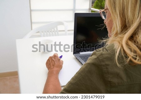 a left-handed woman writes in a notebook with a computer outside. international left handers day Royalty-Free Stock Photo #2301479019