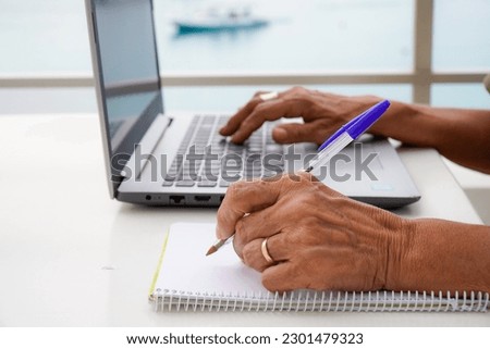 left-handed unrecognizable woman works with the computer and writes in the notebook outside. international left handers day Royalty-Free Stock Photo #2301479323