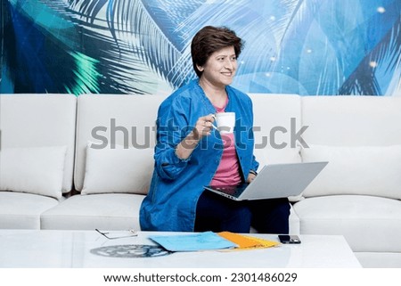 Attractive middle aged woman holding coffee drinking coffee and working on laptop