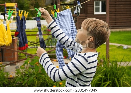 A happy caucasian 9 years boy helps her mother to hang up clothes. Development of fine motor skills through household activities. Selective focus. Royalty-Free Stock Photo #2301497349