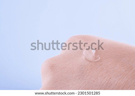 Transparent moisturizer drop of essence, serum or gel on the extra dry skin, close up. Macro photo of woman's hand with gel drop on blue background. SPA concept Royalty-Free Stock Photo #2301501285
