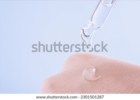Transparent drop of essence, serum or gel drops from the pipette on the  extra dry skin, close up. Macro photo of woman's hand and pipette with gel on blue background. SPA concept. Royalty-Free Stock Photo #2301501287