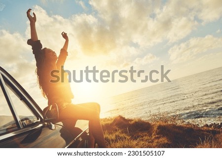 Road trip, sunset and arms raised with a woman at the coast, sitting on her car bonnet during travel for freedom or escape. Nature, flare and water with a young female tourist traveling in summer Royalty-Free Stock Photo #2301505107