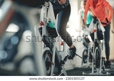 Fitness, legs and exercise bike with people in a gym for a cardio or endurance spinning class workout. Health, wellness and energy with a sporty athlete group training or cycling in a sports center Royalty-Free Stock Photo #2301505137