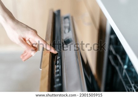 Woman turn on built-in dishwasher to wash dishes in modern kitchen. Choosing energy efficient program on control panel. Concept of rational use of water resources Royalty-Free Stock Photo #2301505915