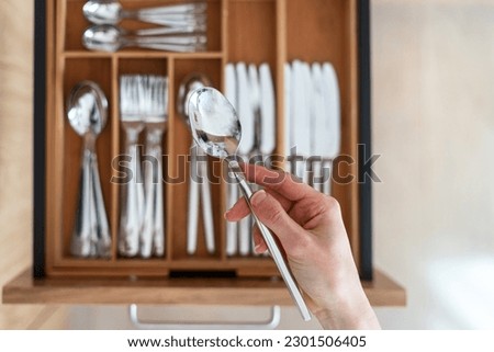 Selective focus on woman hand holding stainless steel spoon against blurred cutlery set in wooden organizer. Tidyness and neat in kitchen drawer. Keeping silverware clean concept Royalty-Free Stock Photo #2301506405