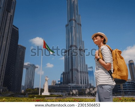Enjoying travel in United Arabian Emirates. Young woman with yellow backpack walking on Dubai Downtown in sunny summer day. Royalty-Free Stock Photo #2301506853