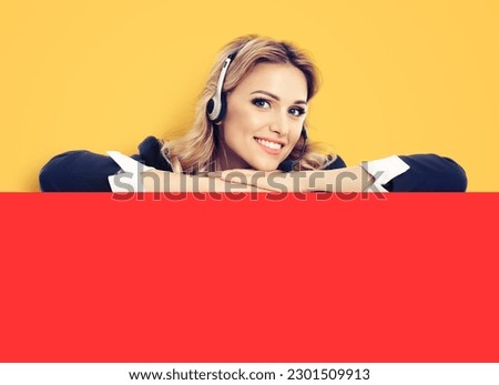Call center. Customer support service female phone operator or sales agent in headset, dark blue confident suit standing behind signboard with copy space area for text, isolated over yellow background