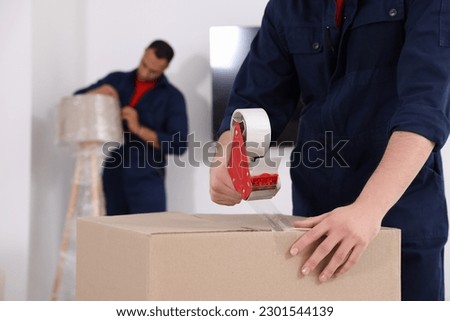 Male mover packing box with adhesive tape in house, closeup. Space for text Royalty-Free Stock Photo #2301544139