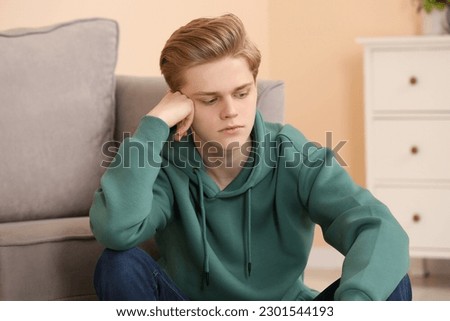 Upset teenage boy sitting alone in room Royalty-Free Stock Photo #2301544193