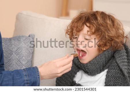 Mother giving cough syrup to her son on sofa Royalty-Free Stock Photo #2301544301