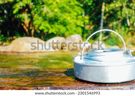 Kettle camping placed on a piece of wood behind the picture is a stream in Thailand, the edge of the screen is used as a back cover,