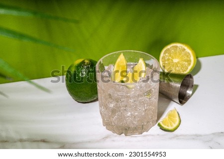 Cold iced Ti punch alcohol cocktail, small punch, rum-based mixed drink with fresh lime slice garnish, on high-colored green background