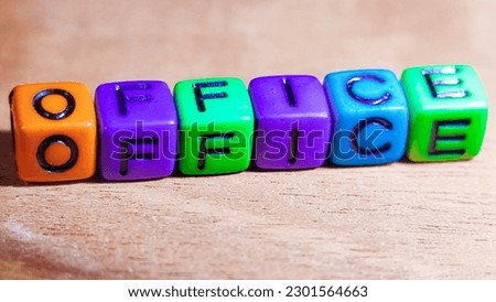The word OFFICE is written in colorful plastic cuboid letters on a wooden background. Job concept