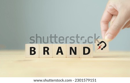 Build brand loyalty concept. Customers continue engaging and purchasing from the same brand, positive feelings toward brand. Wooden cube blocks with BRAND text and magnet icon on clean background. Royalty-Free Stock Photo #2301579151