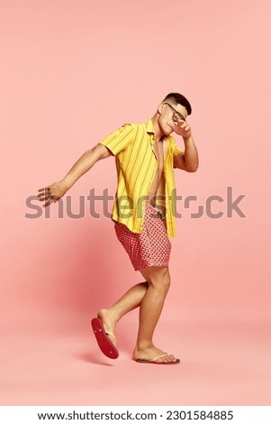 Beach party. Portrait of attractive young guy, student wearing summer clothes and sunglasses dancing over pink studio background. Concept of human emotions, celebrating, vacation, summer, weekend, ad