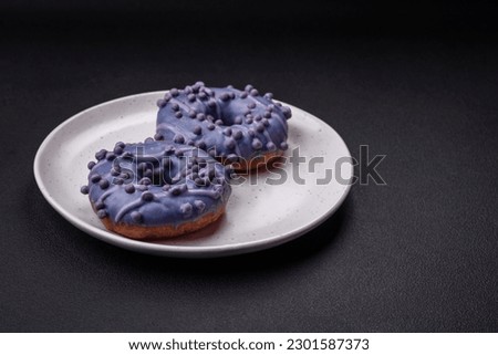 Delicious sweet donut of purple color in glaze and with lilac balls with chocolate filling on a dark concrete background