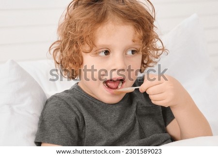 Cute boy taking measuring spoon with cough syrup on bed. Effective medicine Royalty-Free Stock Photo #2301589023