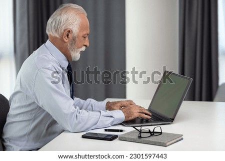 Senior businessman using laptop with green screen sitting by the desk. Confident director or CEO working in his modern office.