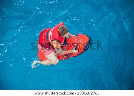 A boy in a red life jacket swims with underwater scooter seabob off the coast of the ANTIPAXOS island, Paralia Voutoumi beach, Ionian Islands, Greece in summer. Horizontal. View from above.