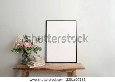 Blank black picture frame mockup. Artistic table, wooden bench still life composition with cup of coffee, old books. Spring bouquett of pink tulips, white daffodils. Hawthorn, guelder roese flowers.