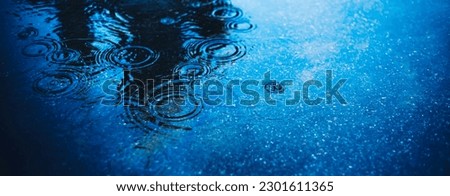 There is a deep puddle on the road asphalt into which raindrops fall and create circles on the water. Bad weather in the city. Background.