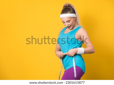 Beautiful young woman measuring her waist with a measuring tape, isolated on yellow background. Weight loss concepts. Vitality girl, healthy body. 80s styling. Studio shot Royalty-Free Stock Photo #2301615877