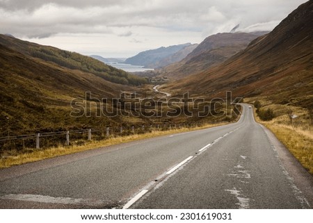 Low angle view of a winding road across a valley leading to a lake surrounded by misty mountains in the Scottish Highlands, United Kingdom