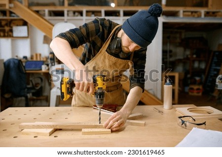 Young man jointer working with drill leaning over table at carpentry workshop Royalty-Free Stock Photo #2301619465