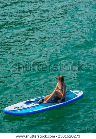 SUP Stand up paddle board. Blond girl rest on paddle board in sea. Aerial view. Woman on summer holidays vacation lifestyle. Mtsvane Kontskhi Beach, Batumi, Georgia.