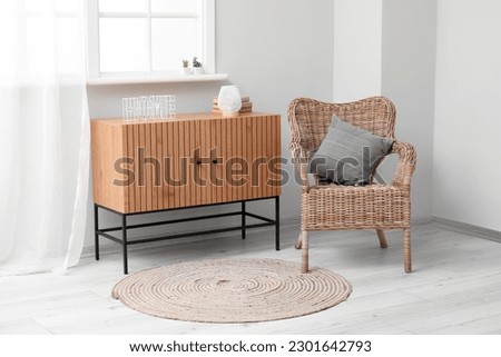 Stylish wooden cabinet and cozy wicker armchair near window