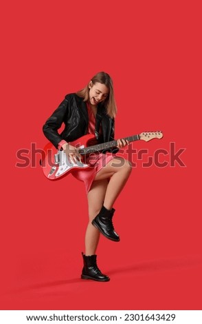 Young woman playing guitar on red background Royalty-Free Stock Photo #2301643429