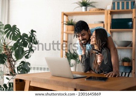Happy affectionate couple shopping online from home using laptop and credit card, making convenient financial e-commerce payment digital transaction, enjoying their time together, planning a trip.