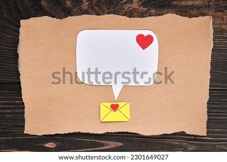 Postcard with email icon, red heart and speech bubble in paper art style. Love letter, greeting card, invitation mockup over dark wooden background. Flat lay, top view, copy space