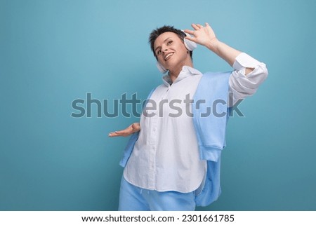 cool young woman with short haircut dancing to a playlist in headphones on a studio background with copy space