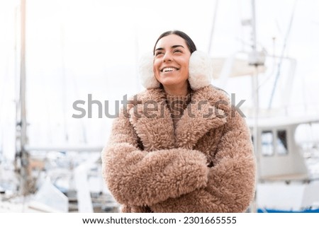 Young woman wearing winter muffs at outdoors looking up while smiling Royalty-Free Stock Photo #2301665555