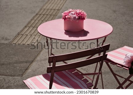small round pink terrace table with flower pot. wood and metal pink foldable patio chairs. outdoor furniture. bright summer scene. abstract view. selective focus. blurred background. wallpaper image.